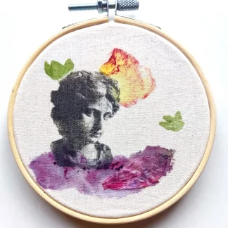 Bastidor circular con retrato en blanco y negro de una estatua griega y manchas de color violeta, rosa y amarillo sobre tela, realizadas con estampación botánica.