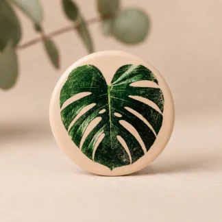 Imán botánico circular de cerámica blanca con ilustración de hoja de monstera verde