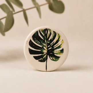 Imán botánico circular de cerámica blanca con ilustración de hoja de monstera deliciosa