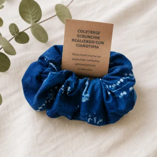 Coletero de cianotipia azul con motivos botánicos sobre fondo textil claro y tarjeta informativa.